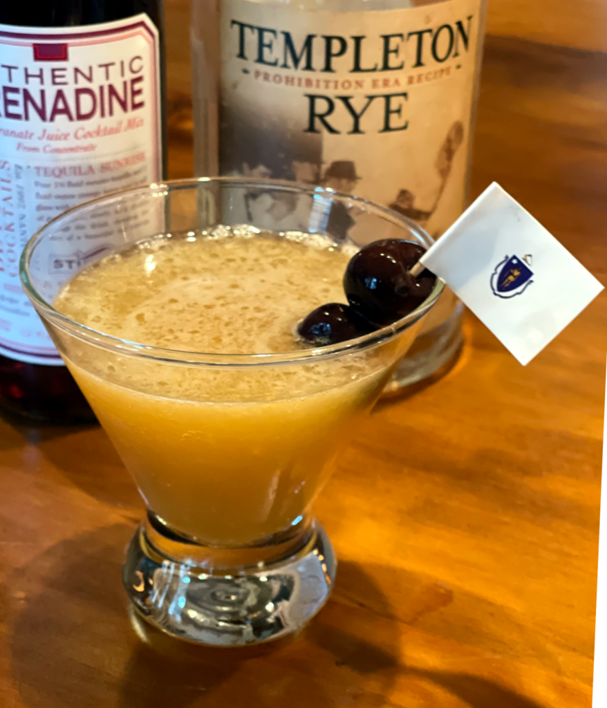 The Ward 8 Cocktail - an orange colored cocktail in a conical glass garnished with two cherries on a small Massachusettes flag